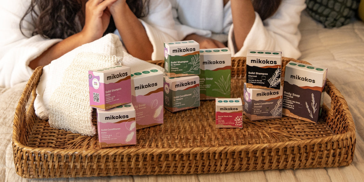 Bandeja con productos Mikokos (shampoo, acondicionador, jabón y mascarilla) junto a dos personas relajándose en batas, día de self-care en casa